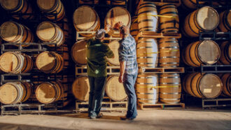 Two people sample whiskey from a wood cask