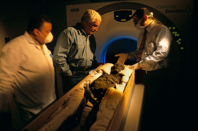 three researchers stand beside Tutankhamun’s mummy in front of a CT machine 
King Tut’s tomb