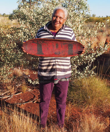 A photo of Anne Rivers holding a long, red, shallow dish with black boab trees painted on the surface