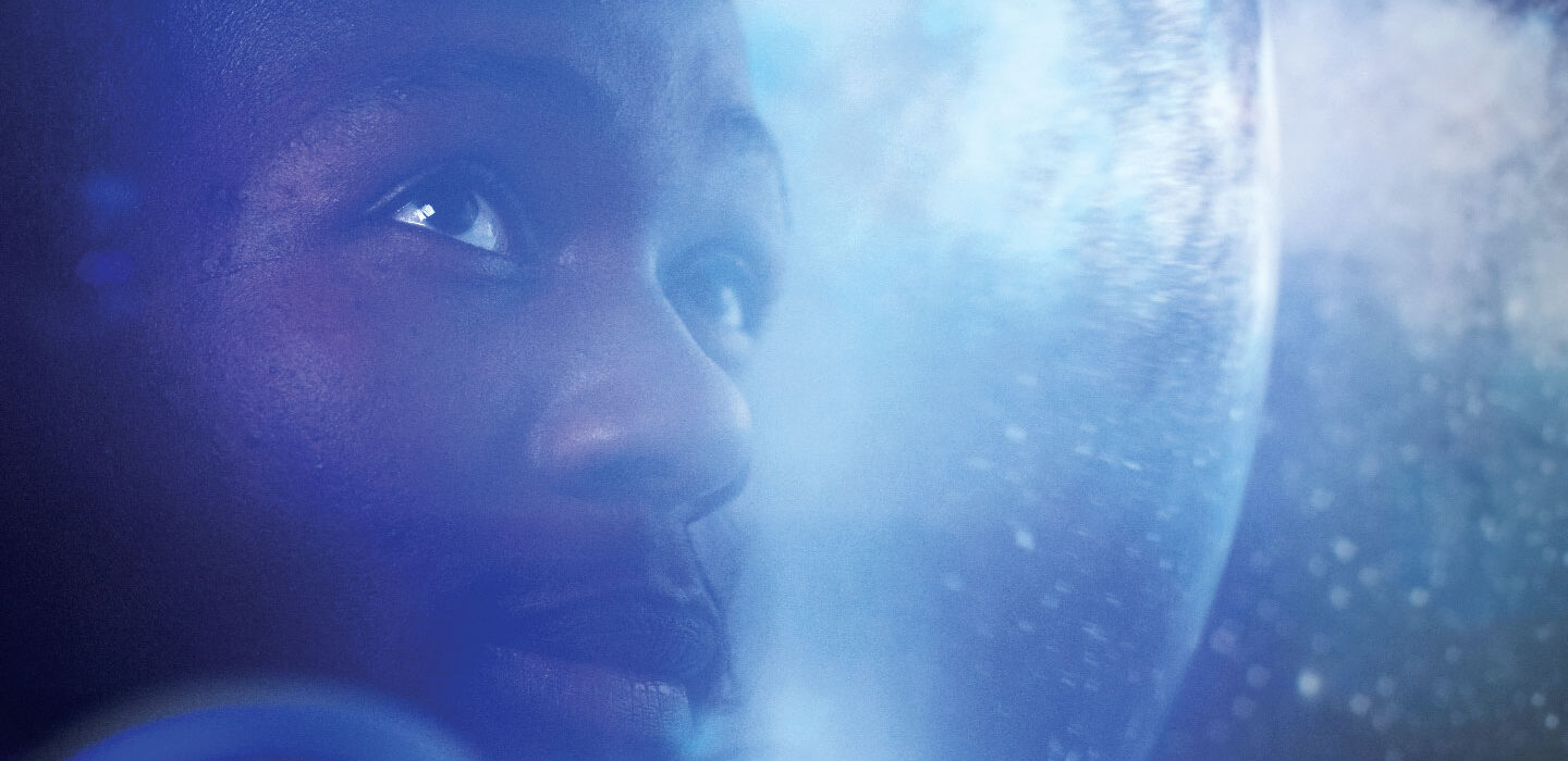 A Black man looks out of an astronaut helmet with outer space in the background