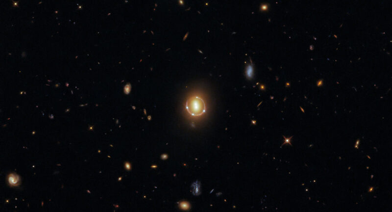 Quasar 2M1310-1714 è visibile come quattro punti di luce attorno a una luce centrale grazie alla lente gravitazionale.  È un'immagine dello spazio in alto.