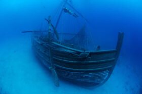An underwater photo of a replica sunken merchant ship with a scuba diver swimming above.