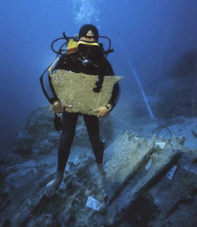 An underwater photo of a diver who participated in excavations of the Uluburun shipwreck holds up a tin ingot.