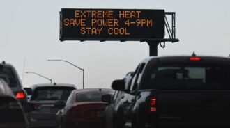 photo of cars backed up on a freeway with a sign above that reads, "EXTREME HEAT SAVE POWER 4-9PM STAY COOL"