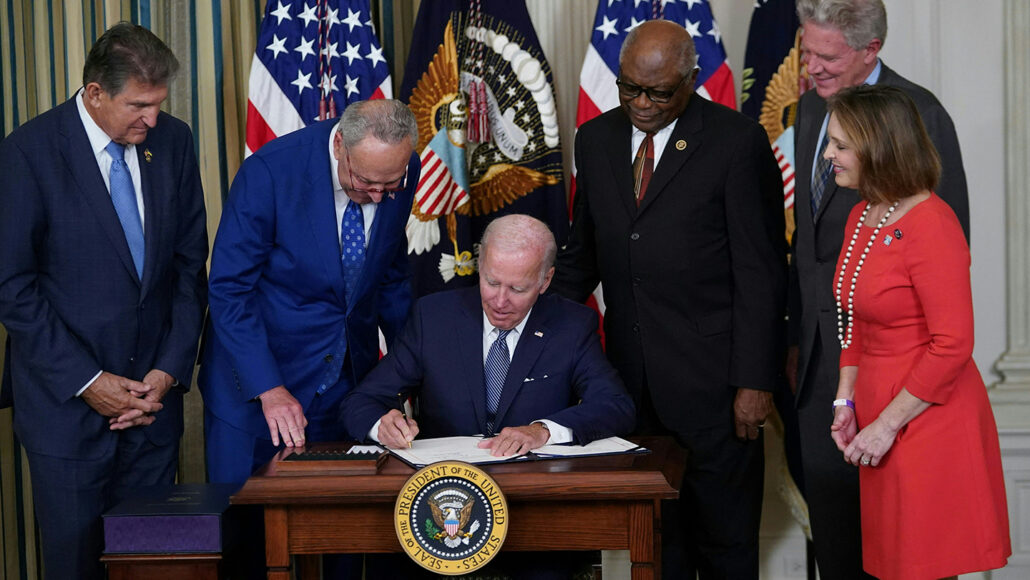 A photo of President Joe Biden signing the Inflation Reduction Act into law with a group of four men and one women standing around him.