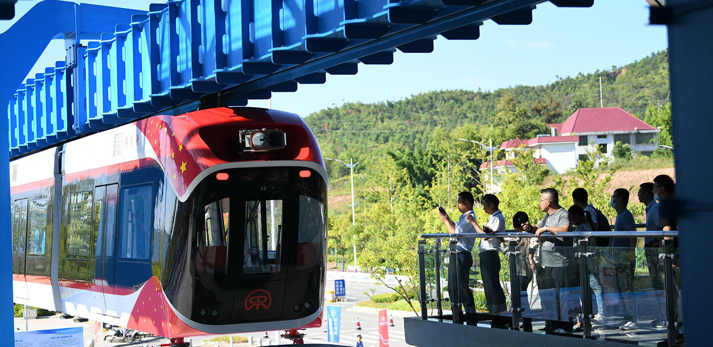 A photo of China's maglev train as it comes into a station with several people standing at balcony of a nearby platform.