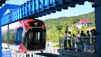 A photo of China's maglev train as it comes into a station with several people standing at balcony of a nearby platform.