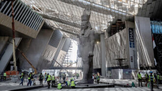 A photo of a giant, 3,200-year-old statue of King Ramses II inside the Grand Egyptian Museum with constructions workers milling about.