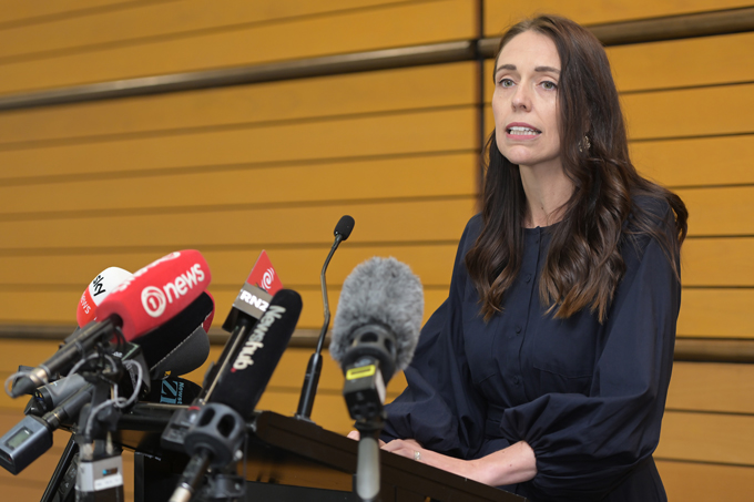 Una foto del primo ministro neozelandese Jacinda Ardern in piedi su un podio con diversi microfoni che annunciano le sue dimissioni.