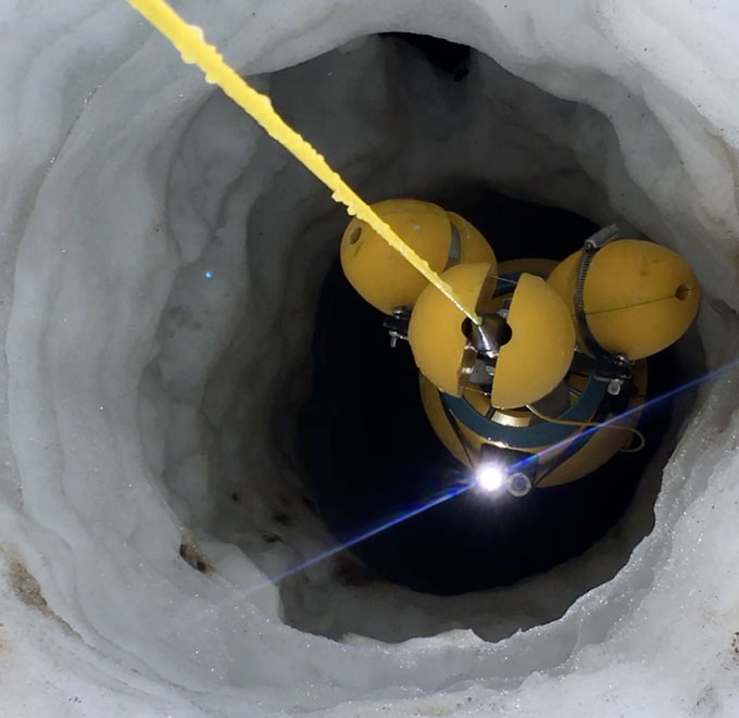 A photo of a yellow remote-operated vehicle being lowered down a borehole into the ice of the Thwaites Glacier.