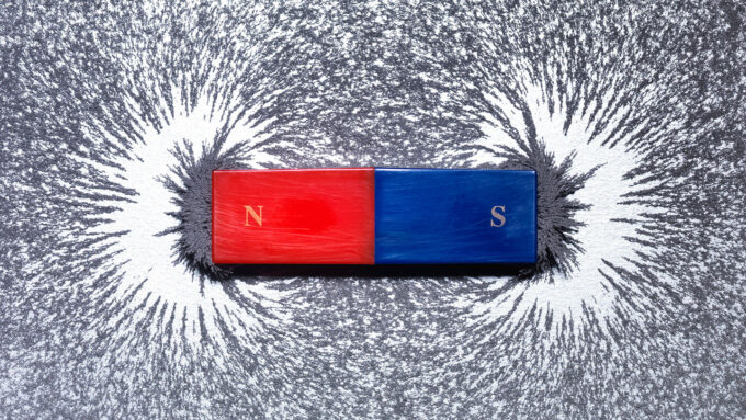 A red and blue magnet bar on a background of metal shavings with the nearby shavings attracted to the ends of the magnet.