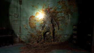 A still image from the television show The Last of Us showing a human body that has been completely covered by an orange fungus attached to a gray wall.