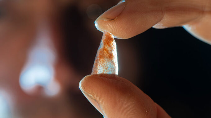 A closeup photo of a small semi-transparent stone in the shape of an arrowhead held between a person's index finger and thumb.