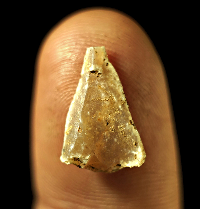 A close up photo of of a small semi transparent stone triangle resting on an adult's fingertip.