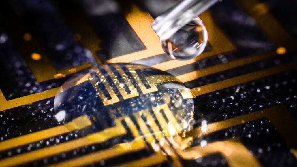 A close up photo of a clear liquid forming a bubble on what appears to be a black and gold circuit board.