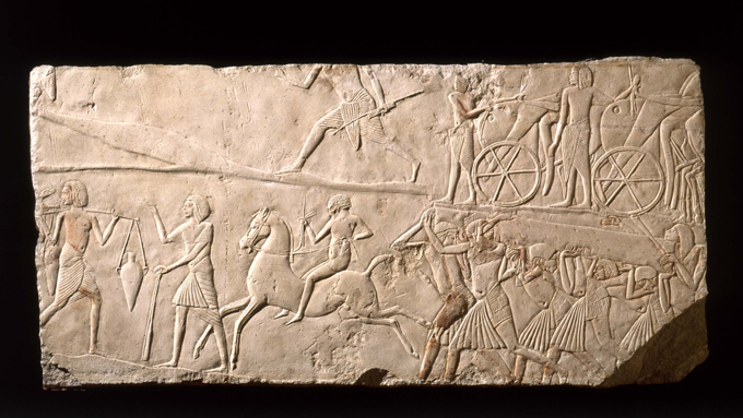 A photograph of a limestone relief showing someone bareback riding a horse while others go about various tasks.