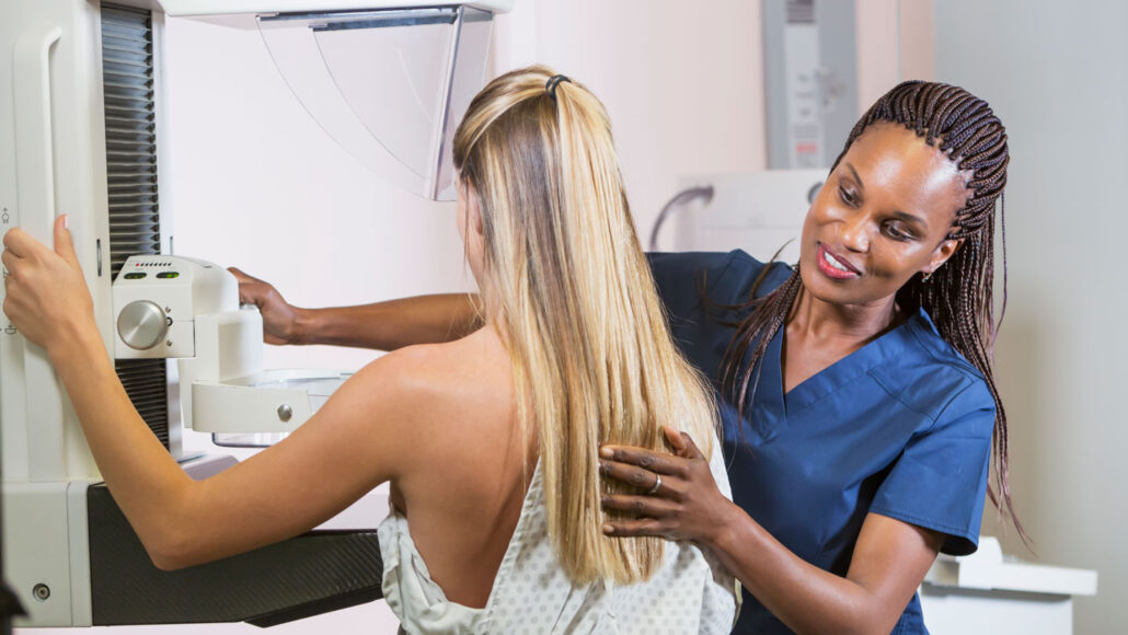 A photo of a woman getting a mammogram while a doctor helps position her with the machine.