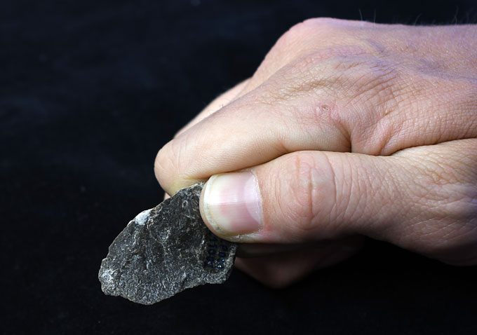 A photo of a hand holding black oval-shaped stone shard.