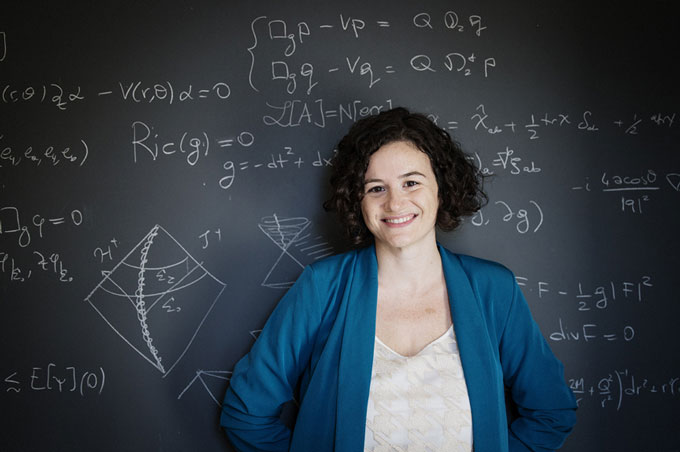 A photo of Elena Giorgi standing in front of a blackboard with mathematical equations written in white chalk.