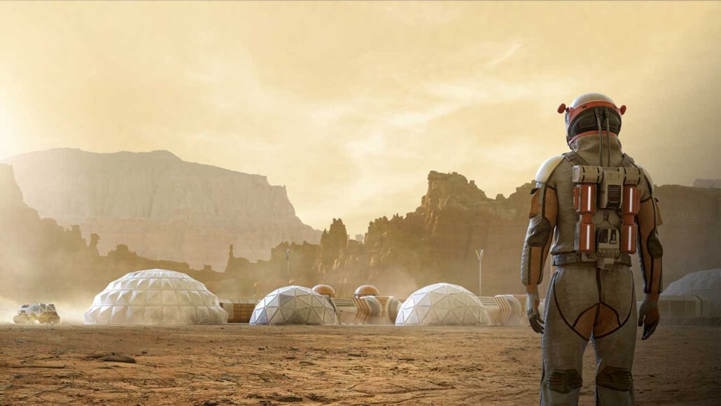 An astronaut in a space suit stands with their back to the camera and looks out at inflatable domes as part of a habitat on Mars.