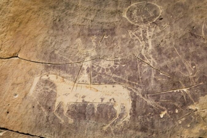 Ein Foto der Felskunst, das ein Pferd und einen Reiter zeigt, die in den Fels geritzt sind. 