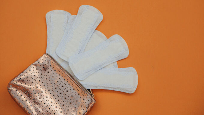 A photo of several maxi pads spread out of a small bag on an orange background.