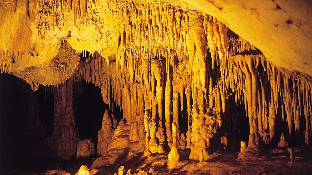 A photo of the inside of cave with stalagmites and stalactites in a yellow light.