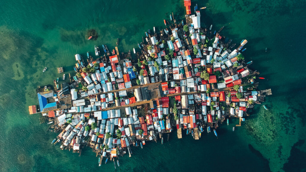 An overhead photo of the many different and brightly colored homes all clustered together on a small island while surround by a green sea.