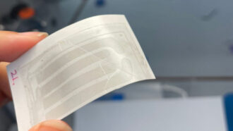 article material science A photo of a hand holding a light colored rectangle with darker lines running across it.