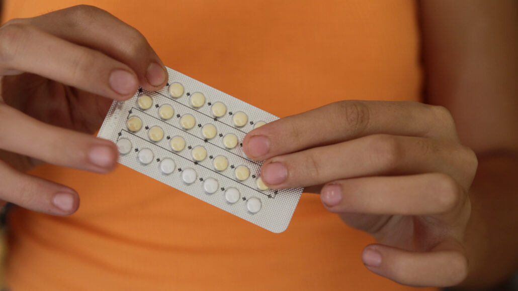 A photo of a woman holding a packet of birth control pills with two hands in front of her torso.