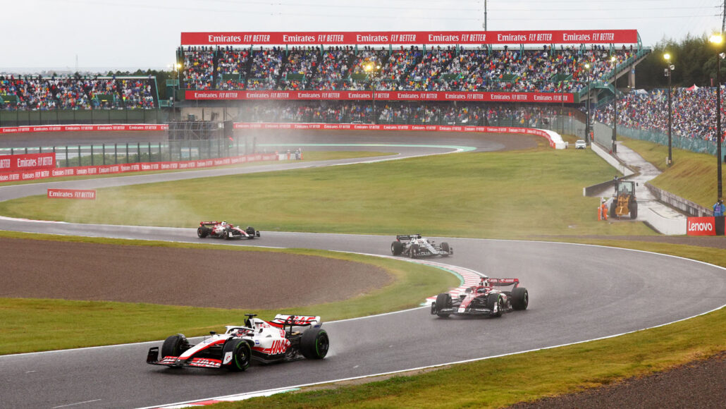 A photo of several Formula cars driving on a curvy race track with stands full of people in the distance.