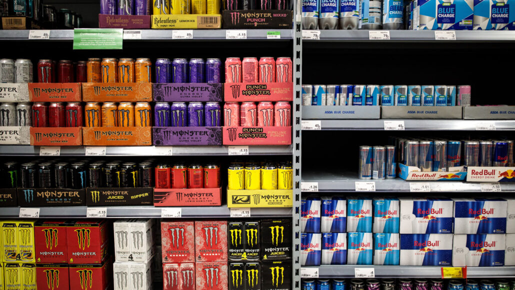 A photo of several different flavors of Monster, Red Bull and other energy drinks sitting on grocery store shelves.