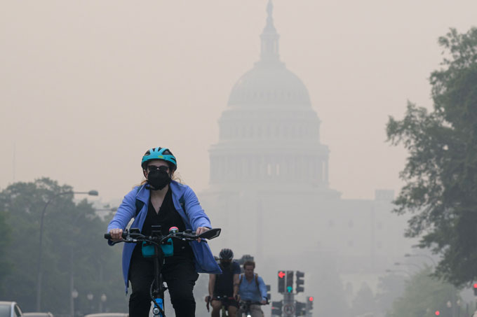 A photo of a biker wearing a mask while the U.S. Capitol building can barely be seen in the background through a haze.