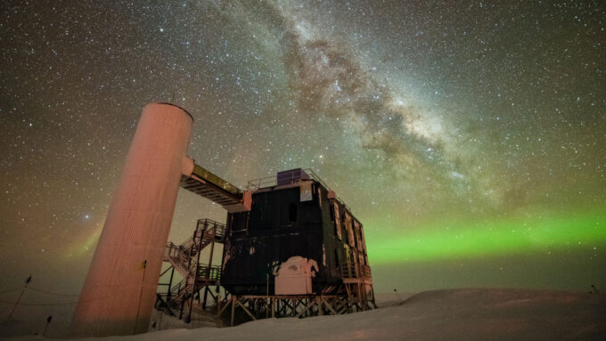 A photo of the IceCube neutrino detector in Antarctica with a view of the Milky Way and aurora australis lights.