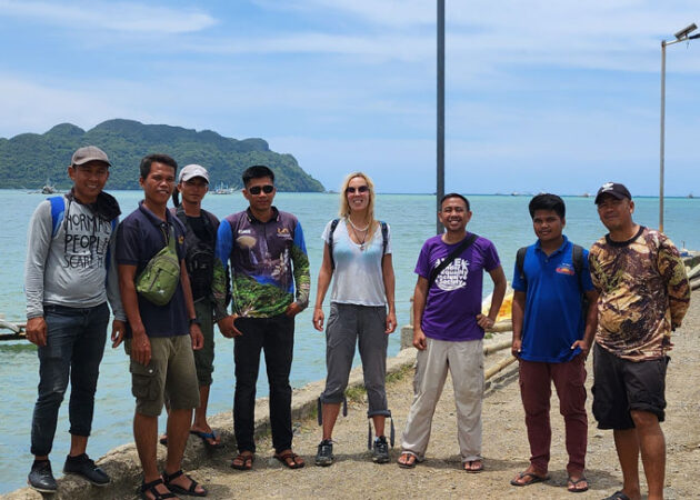 A photo of archaeologist Hermine Xhauflair (center) and colleagues gathered on the island of Palawan in the Philippines with the ocean and another island in the background.