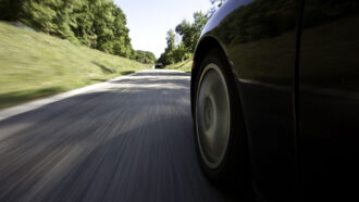 article material science A close up photo of a car's tire while it drives on a black top road.