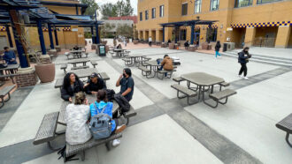 A photo of an outdoor space with tables with a few university students sitting at some of the tables.