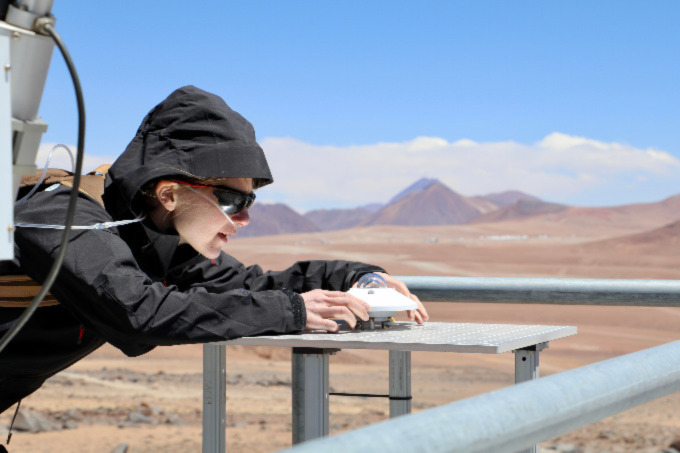 A photo of a researcher working high in the Andes Mountains of Chile sets up an instrument to measure solar radiation.