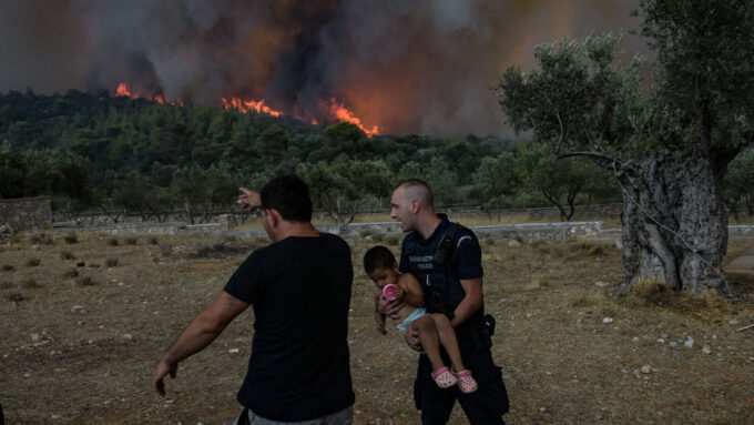 Two men, one holding a child, stand with a wildfire burning in the background