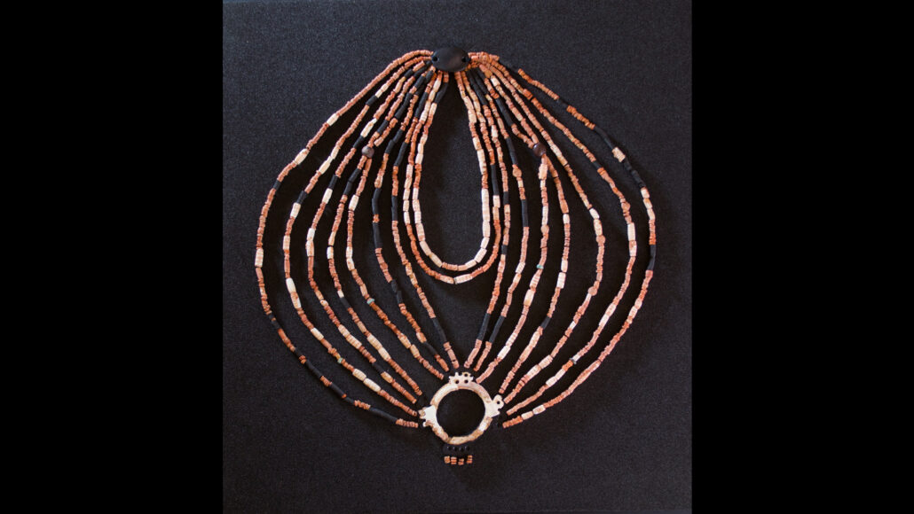 An ornate neckleace made of multiple symmetrical strings of beads, with a pendant and mother-of-pearl-ring at opposite ends