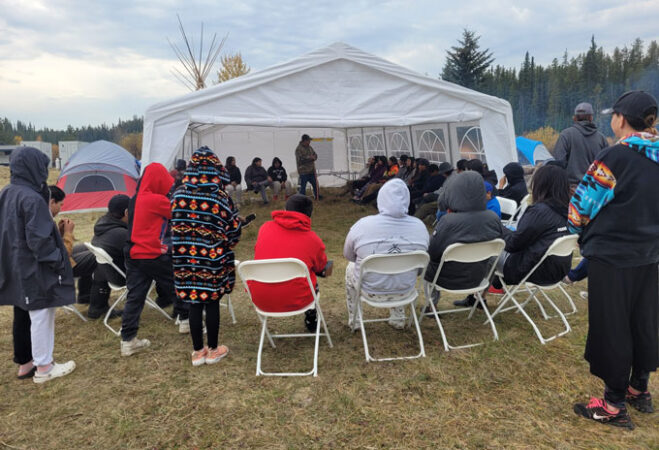 A photo of Indigenous youth sitting around in a circle at a hunting camp in Alberta, Canada.
