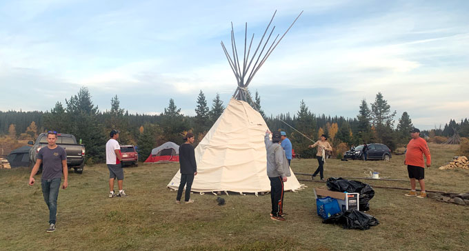 A photo of Indigenous youth putting up a tipi as part of a hunting camp.