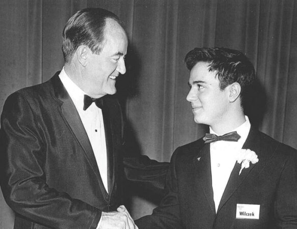 Frank Wilczek, pictured on the right, shakes hands with then-Vice President Hubert Humphrey. Both wear tuxedos in the black and white photo.