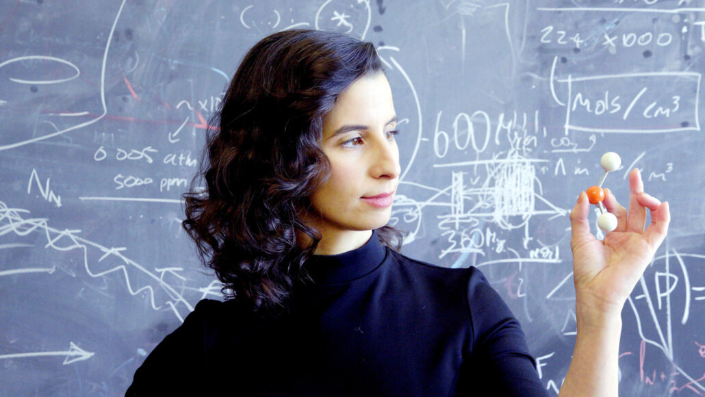 Quantum astrochemist Clara Sousa-Silva stands in front of a blackboard, holding a molecular model in her hand.