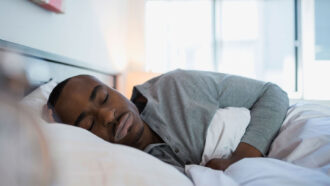 A photo of a black man sleeping on his side facing the camera.
