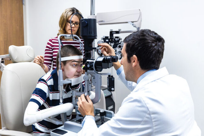 Antonio Vento leans in and looks into an ophthalmoscope as a doctor examines his eyes while his mom looks on in the background.