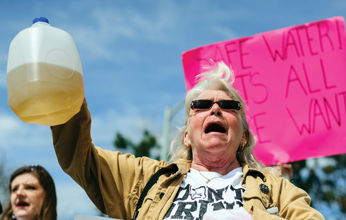 A person holds a jug of brown water with a pink