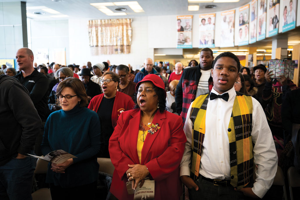 People stand singing in a big room with white walls.