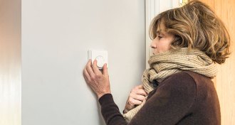 woman bundled up in scarf adjusting thermostat