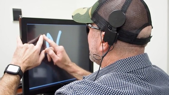 man standing at a screen drawing a letter with his fingers